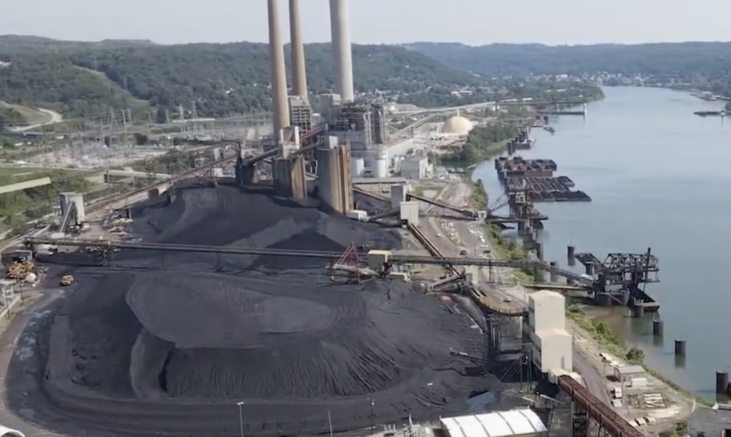 Aerial view of a coal plant by a river with smokestacks and huge piles of coal